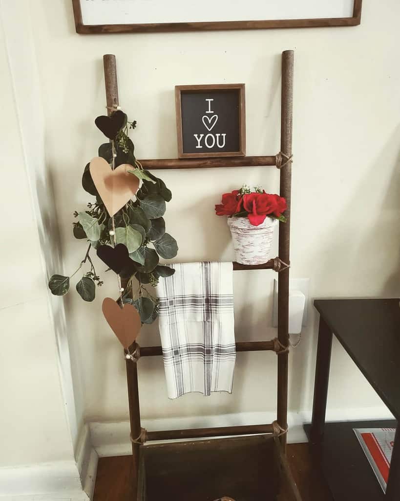 Rustic entryway decor with a wooden ladder shelf, heart garland, greenery, a plaid towel, and a framed 'I love You' sign for a cozy touch