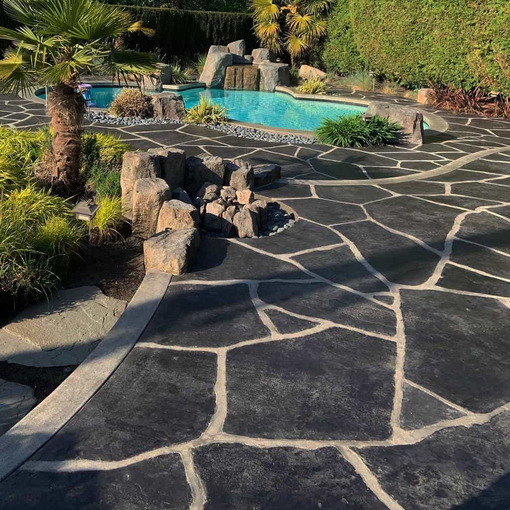 Backyard with a stone patio, palm tree, and a turquoise pool surrounded by rocks and greenery