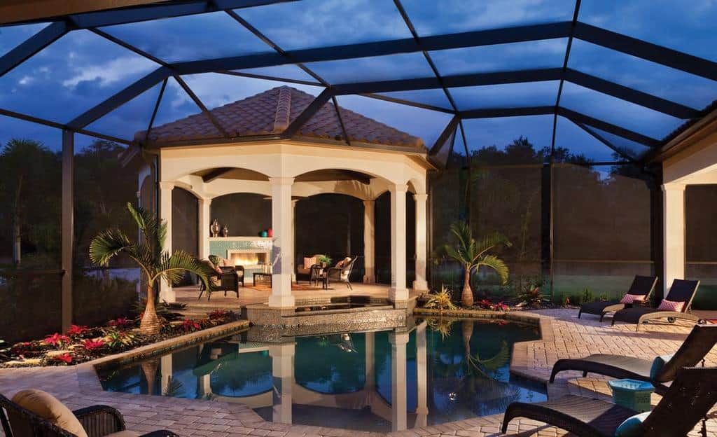 Enclosed patio with a swimming pool, lounge chairs, and a covered seating area under a gazebo, surrounded by tropical plants at dusk