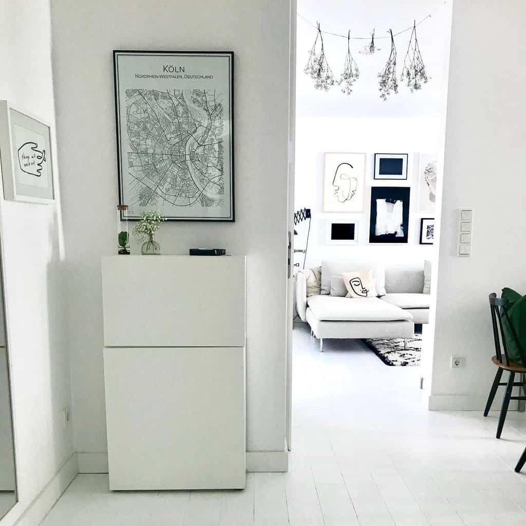 Minimalist entryway with a sleek white shoe cabinet, framed city map, and modern decor leading into a stylish living space