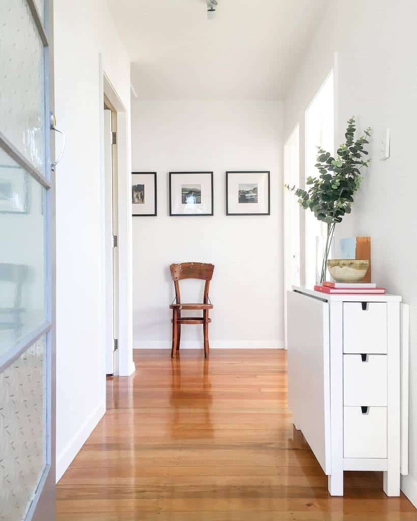 Minimalist entryway with a slim white shoe cabinet, eucalyptus decor, hardwood floors, and framed artwork for a clean, modern look