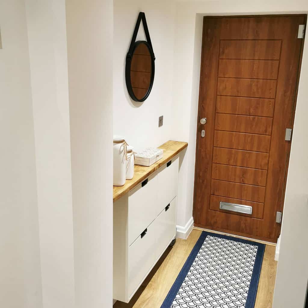 Modern entryway with a sleek white shoe cabinet, wooden countertop, round mirror, and warm wood door for a cozy yet functional look