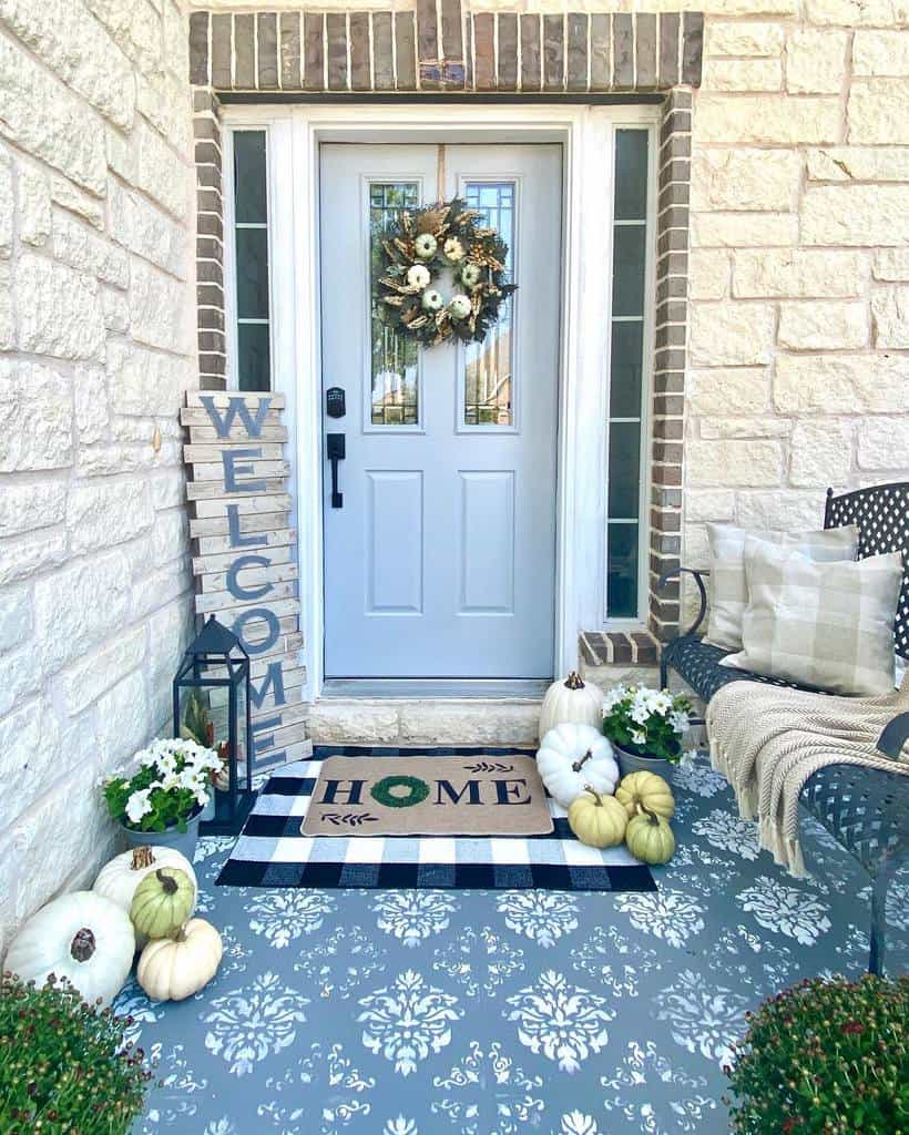 Charming fall-themed porch with pumpkins, a "Welcome" sign, floral wreath on the door, and a "Home" doormat on patterned flooring