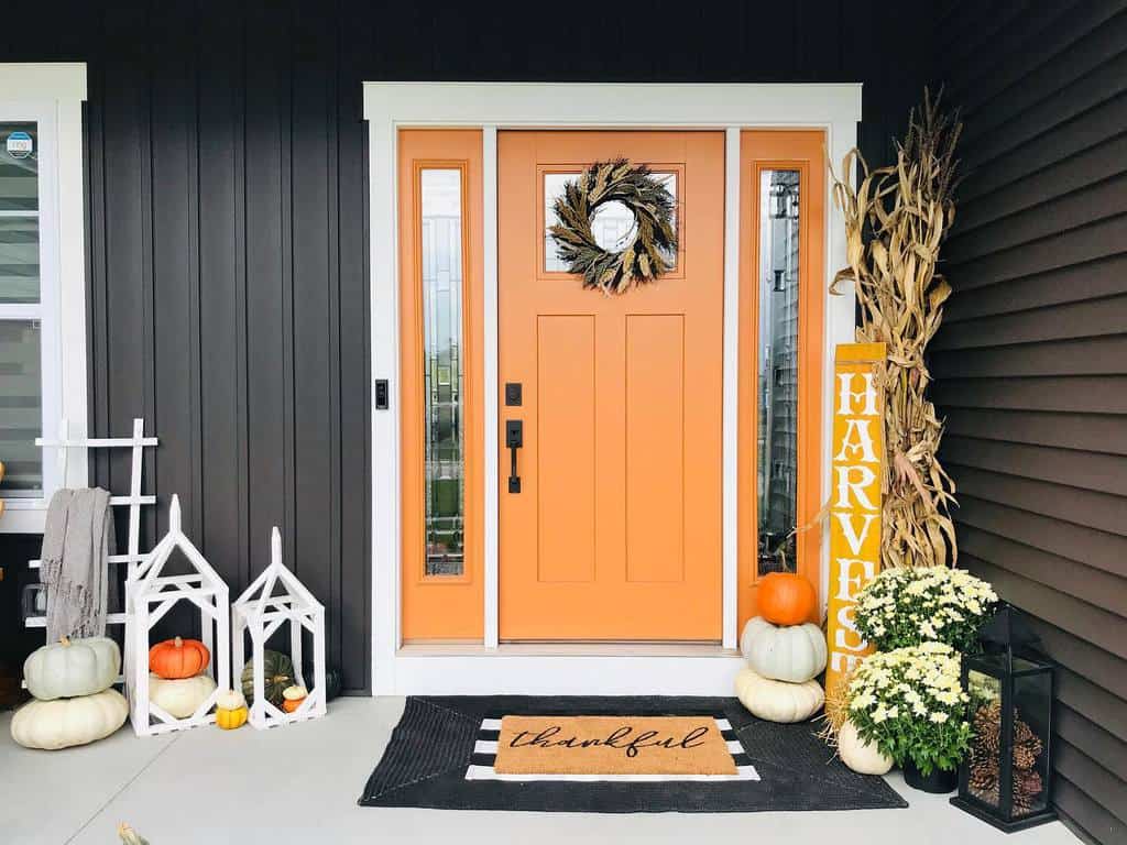 Front porch with an orange door, fall wreath, pumpkins, lanterns, "Harvest" sign, and a welcome mat with "thankful" text