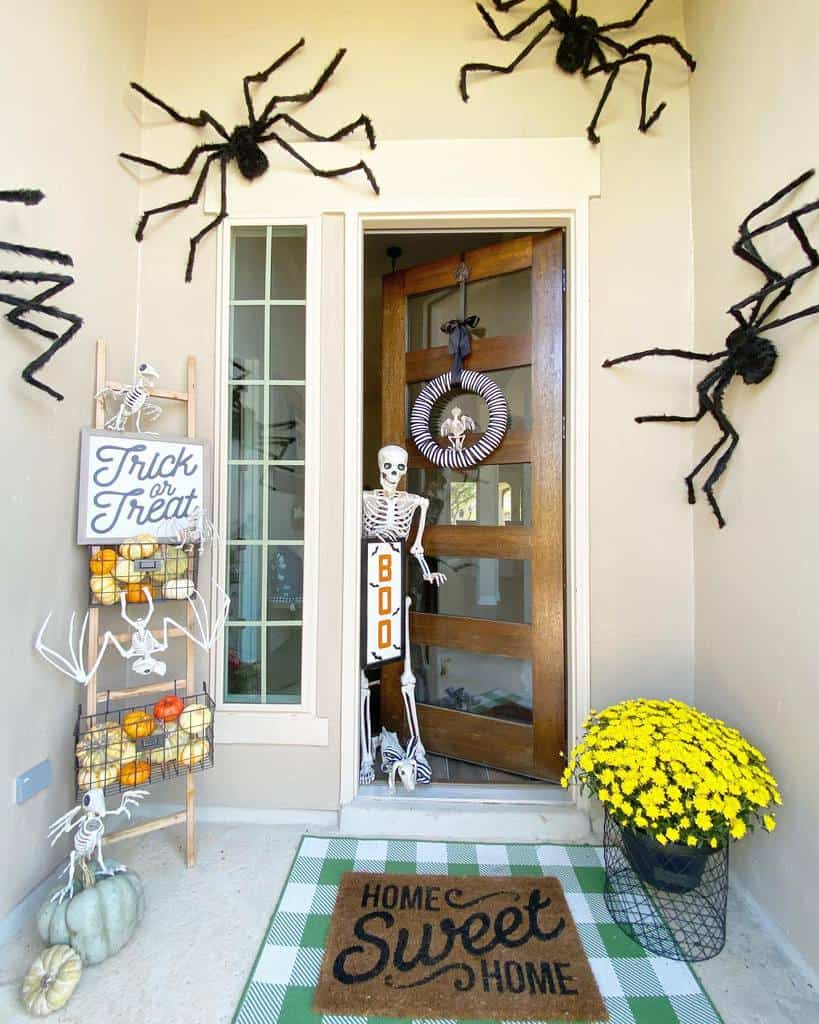 Front door decorated for Halloween with fake spiders, a skeleton, pumpkins, and a "Home Sweet Home" doormat