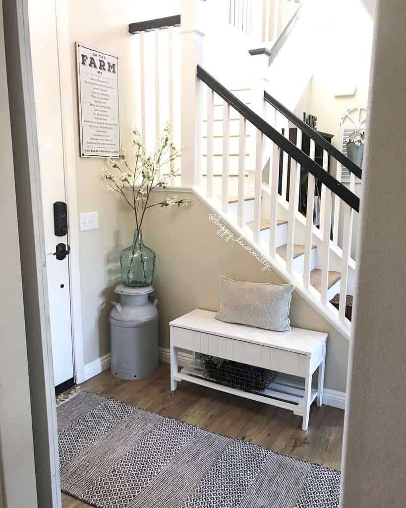 Farmhouse-style entryway with a white bench, rustic decor, a vintage milk can vase, and a cozy striped rug under a staircase