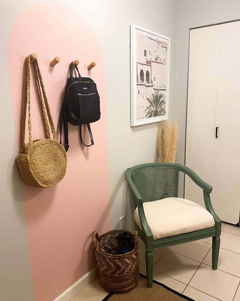 Entryway with a green chair, woven basket, pink wall accent, hanging bags, and framed art; neutral tones and minimal decor