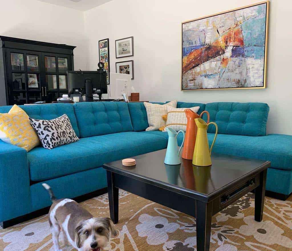 Black wooden coffee table styled with colorful pitchers, set in a vibrant living room with a bold blue sectional sofa and eclectic decor