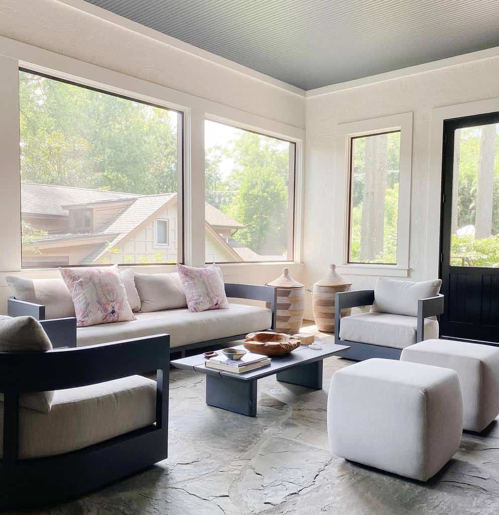 Low-profile modern coffee table with a sleek dark finish, styled with books and decor, set in a bright sunroom with large windows and neutral seating