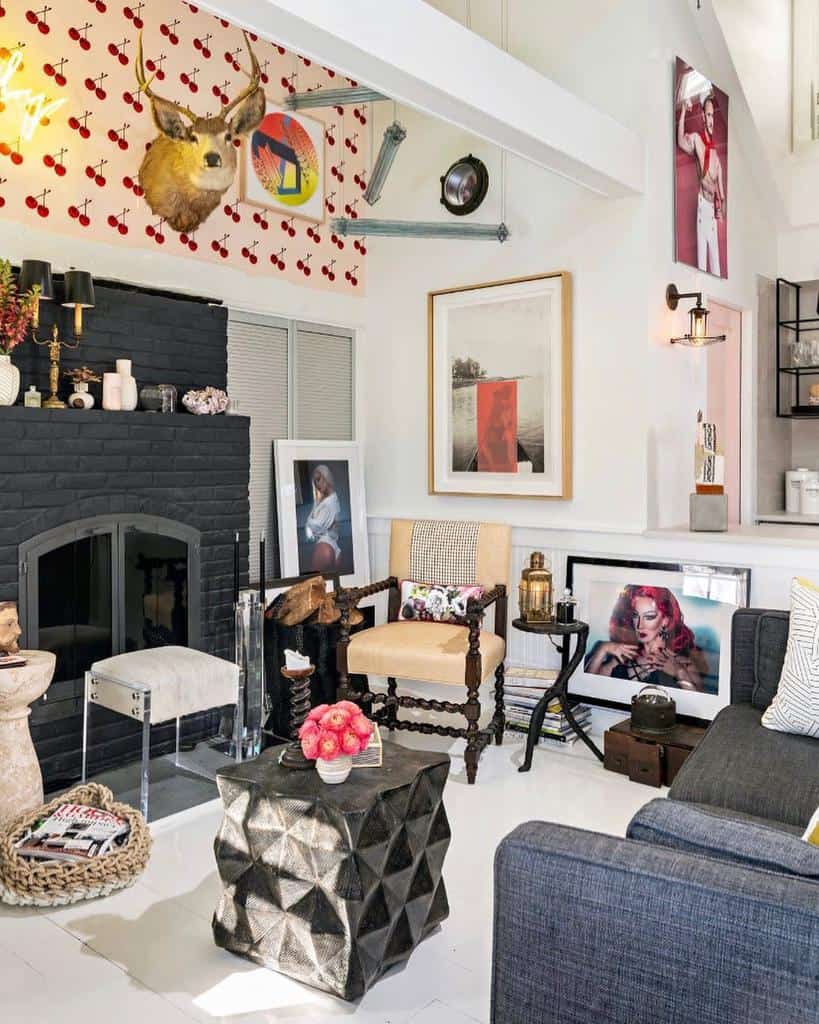 Eclectic living room with dark fireplace, patterned wallpaper, diverse art, geometric table, and assorted chairs under exposed beams