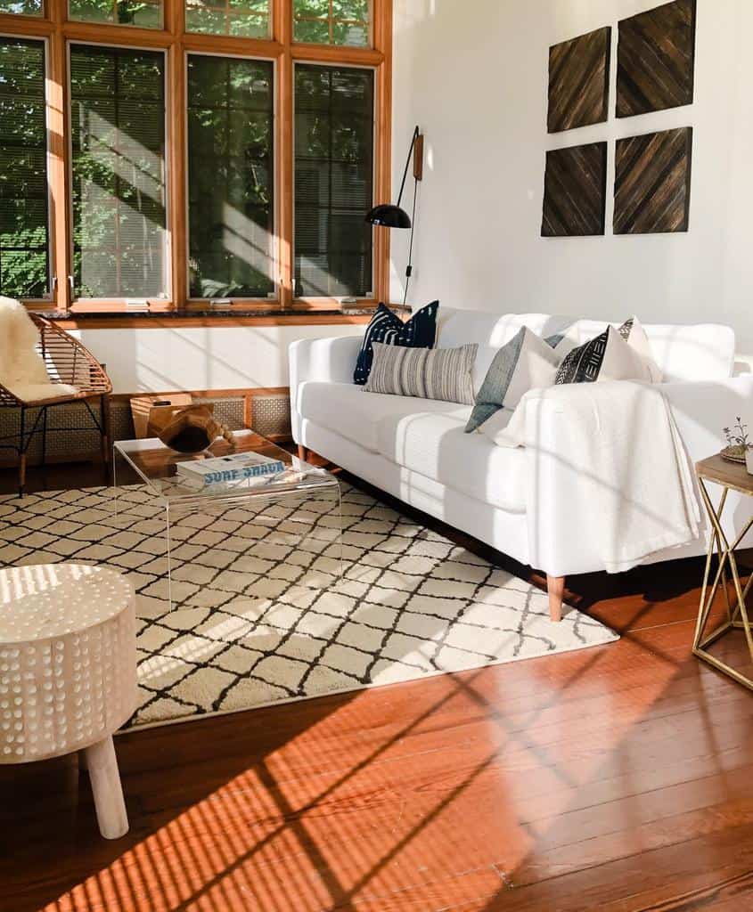 Minimalist clear acrylic coffee table styled with books and wooden decor, set in a sunlit modern living room with a cozy white sofa and geometric rug