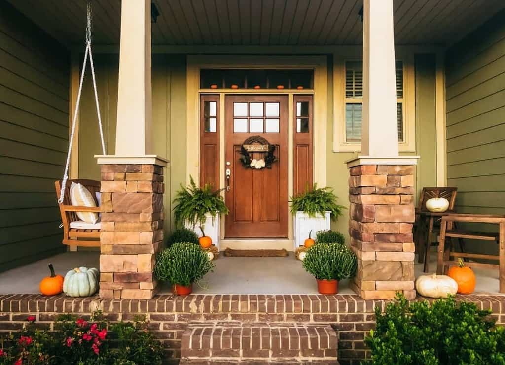 A front porch with a wooden door, swing, pumpkins, and potted plants decorated for autumn with a welcoming atmosphere