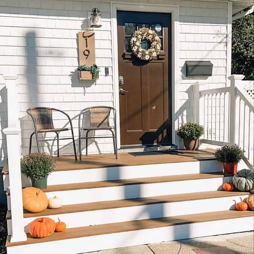 Cozy front porch with autumn decor: pumpkins, potted plants, chairs, and a wreath on the door