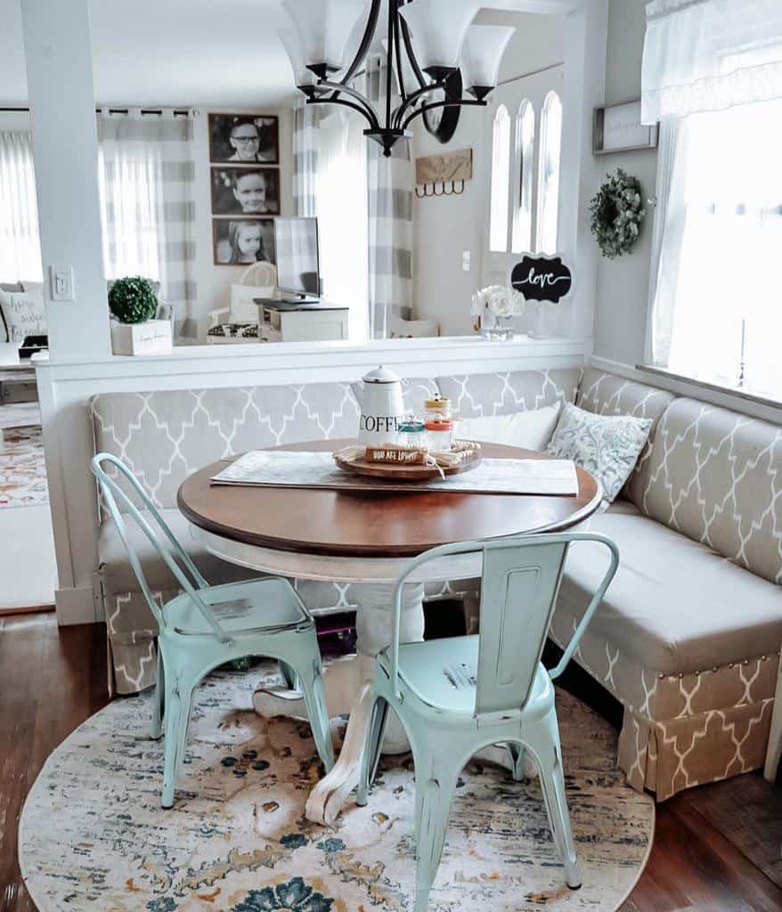 Cozy dining nook with a round table, light blue metal chairs, patterned bench seating, and a chandelier above featuring decor including a "Love" sign.