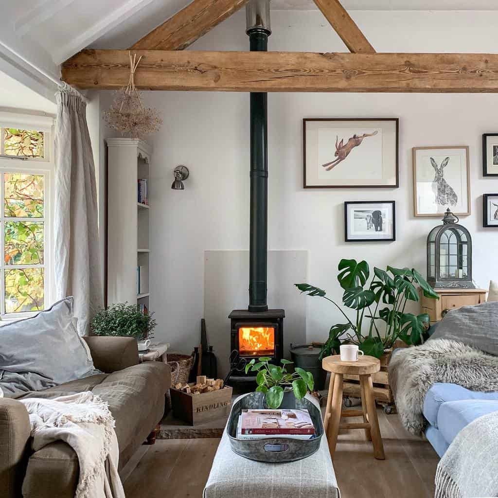 Small living room with a wood-burning stove, wooden beams, plants, and framed art on the walls; soft lighting and comfortable seating.