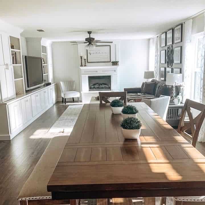 Bright living room with a wooden table and white chairs, built-in shelves, a cozy fireplace, and a gallery wall with framed art.