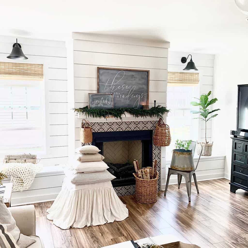 Cozy living room with a fireplace, wood floors, white walls, potted plant, and a cushioned chair. Decor includes baskets and greenery.