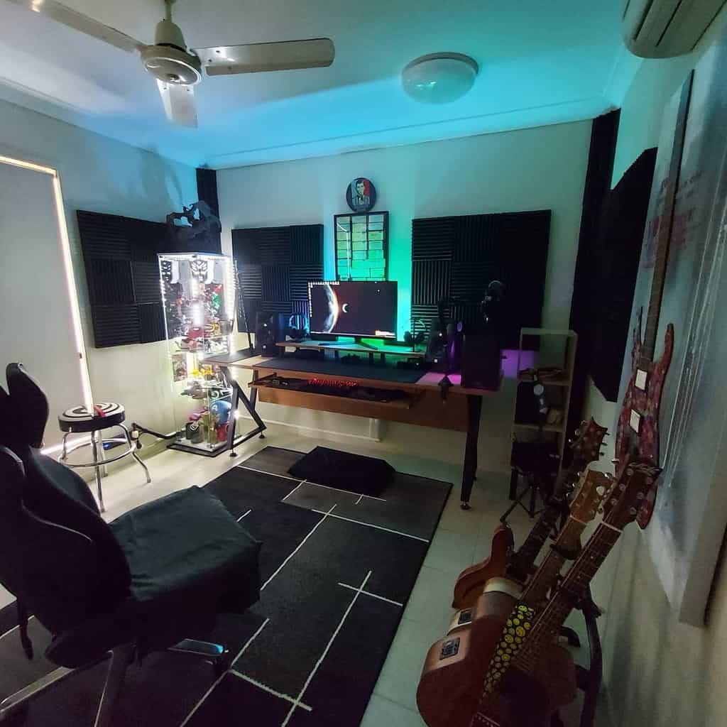 Modern music studio with guitars, a gaming desk, acoustic panels, LED lighting, and a sleek setup for music production and recording