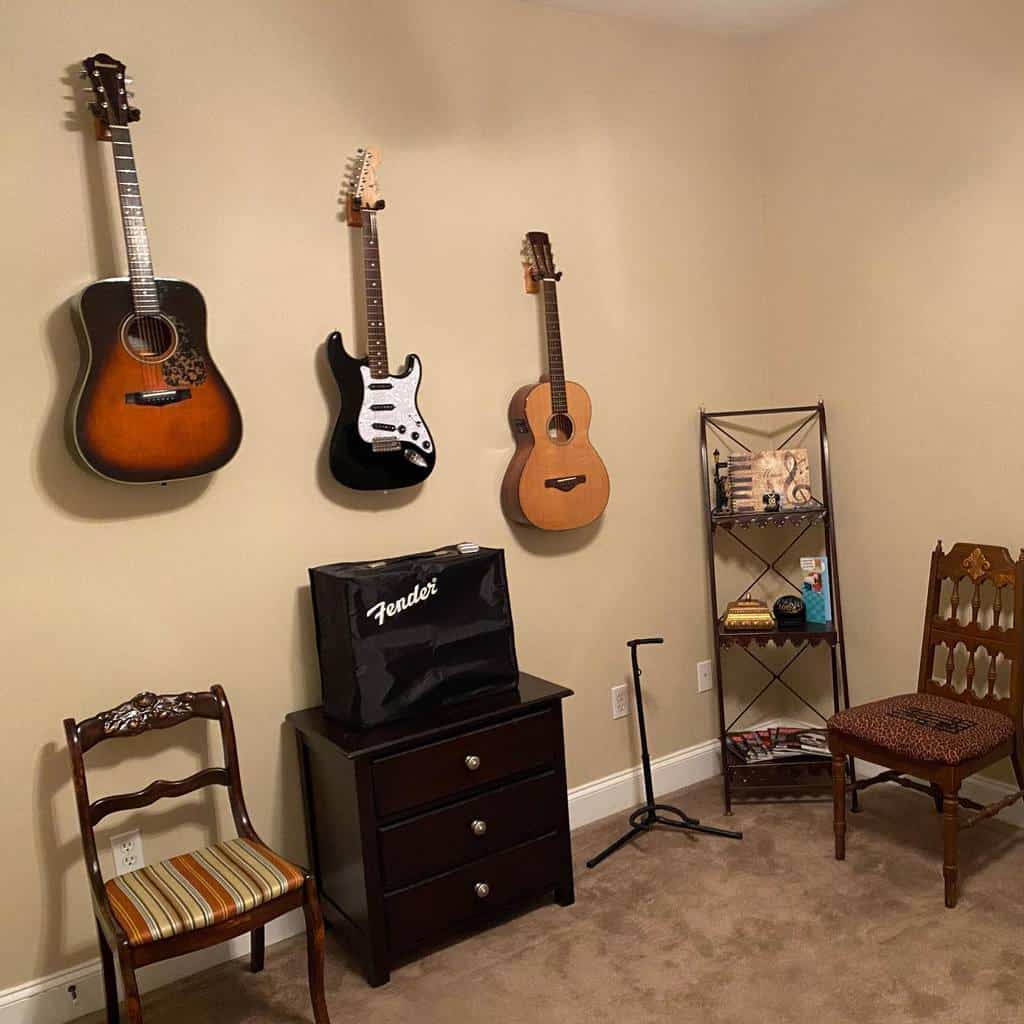 Simple music room with wall-mounted guitars, a Fender amp, vintage chairs, a small bookshelf, and a cozy neutral color scheme