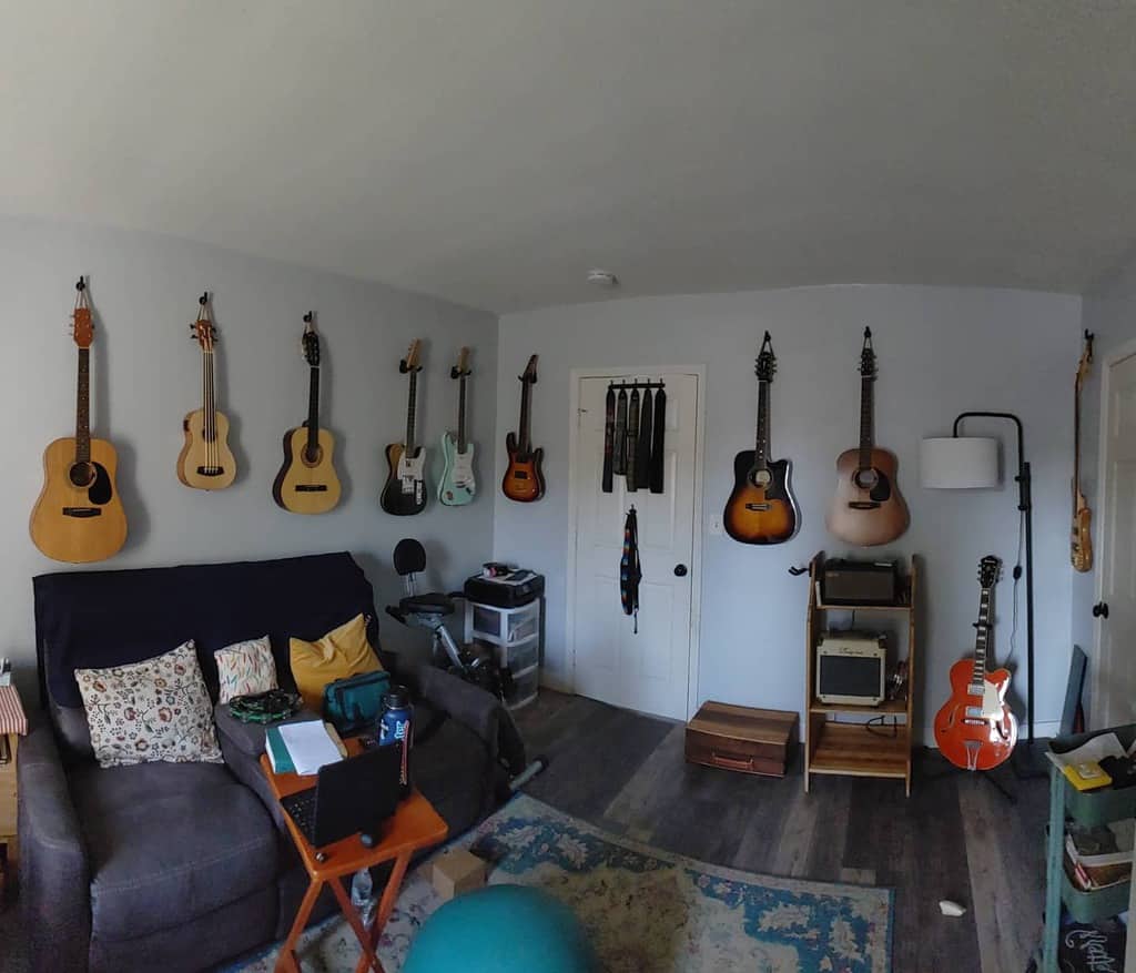 Cozy music room with wall-mounted guitars, a plush sofa, a home workstation, an amplifier, and a relaxed, creative atmosphere