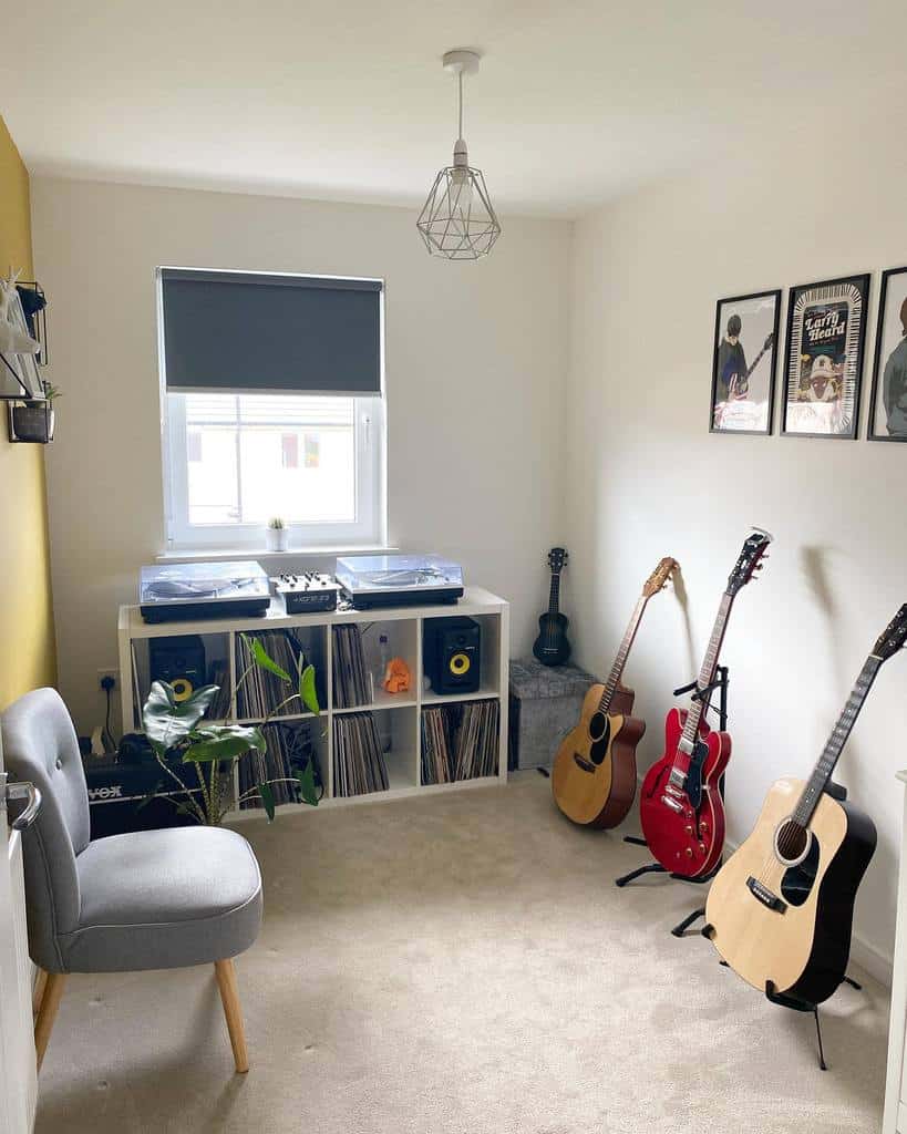 Minimalist music room with guitars, turntables, vinyl records, framed music posters, a cozy chair, and natural light from a window