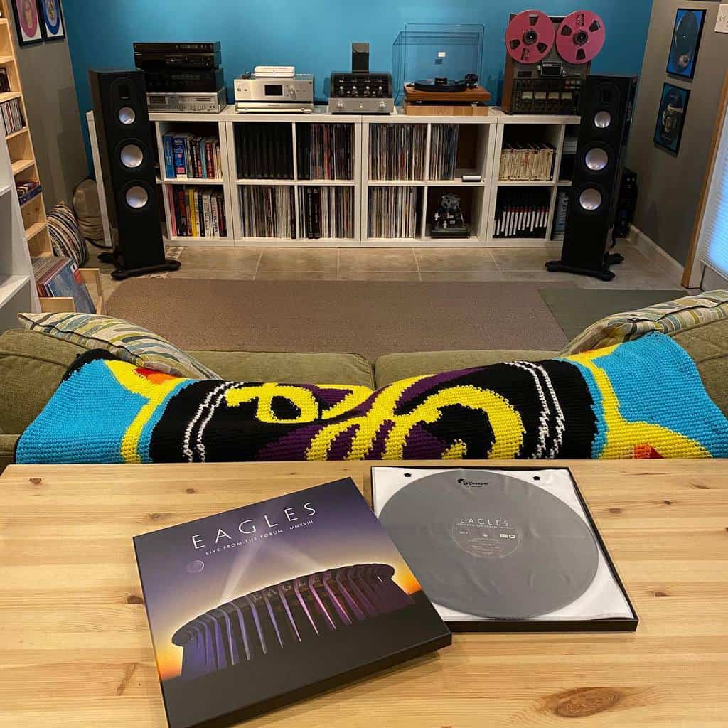 Cozy vinyl listening room with a record collection, turntable setup, large speakers, and an Eagles album on a wooden table