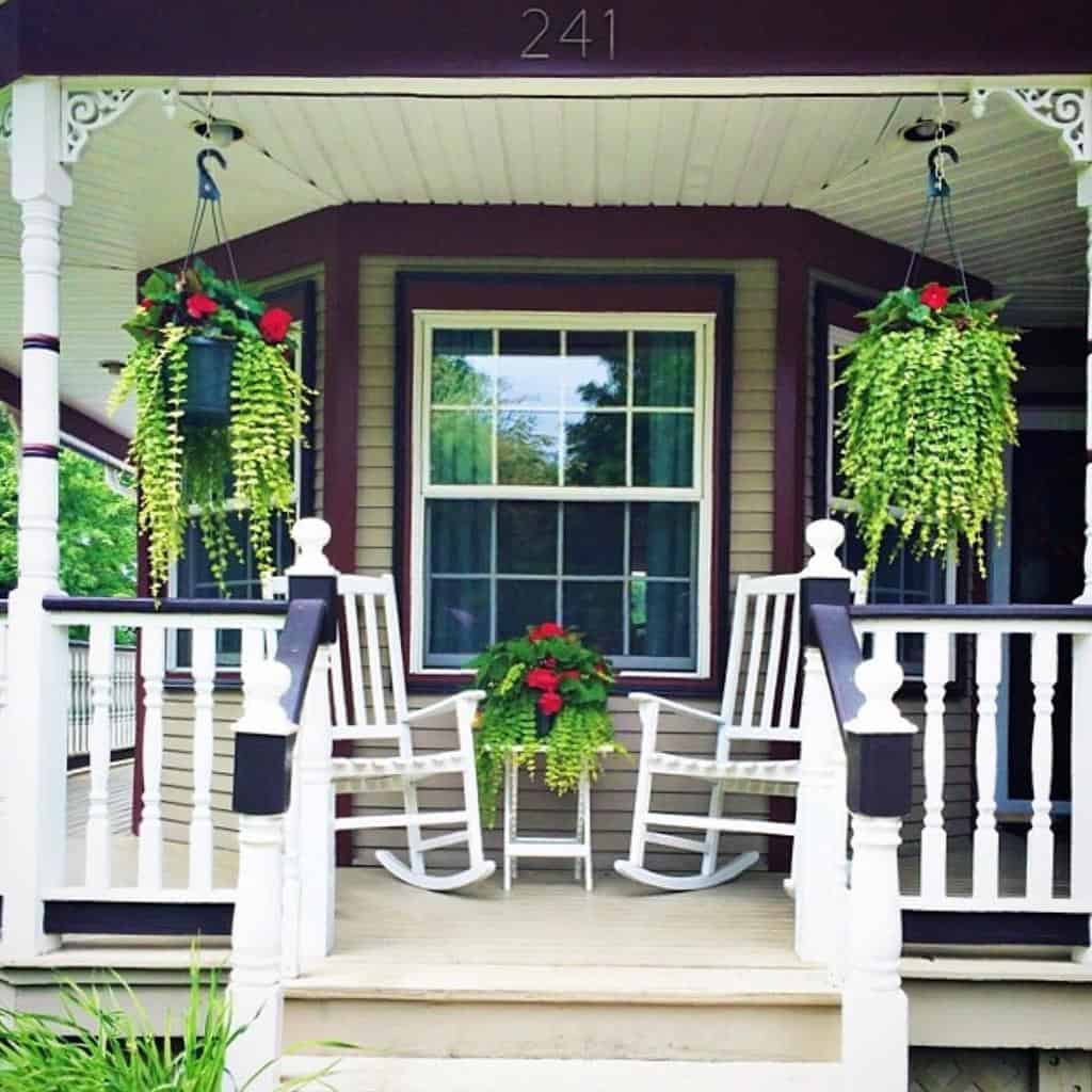 Charming porch with two white rocking chairs, hanging plants, and a potted plant in front of a window