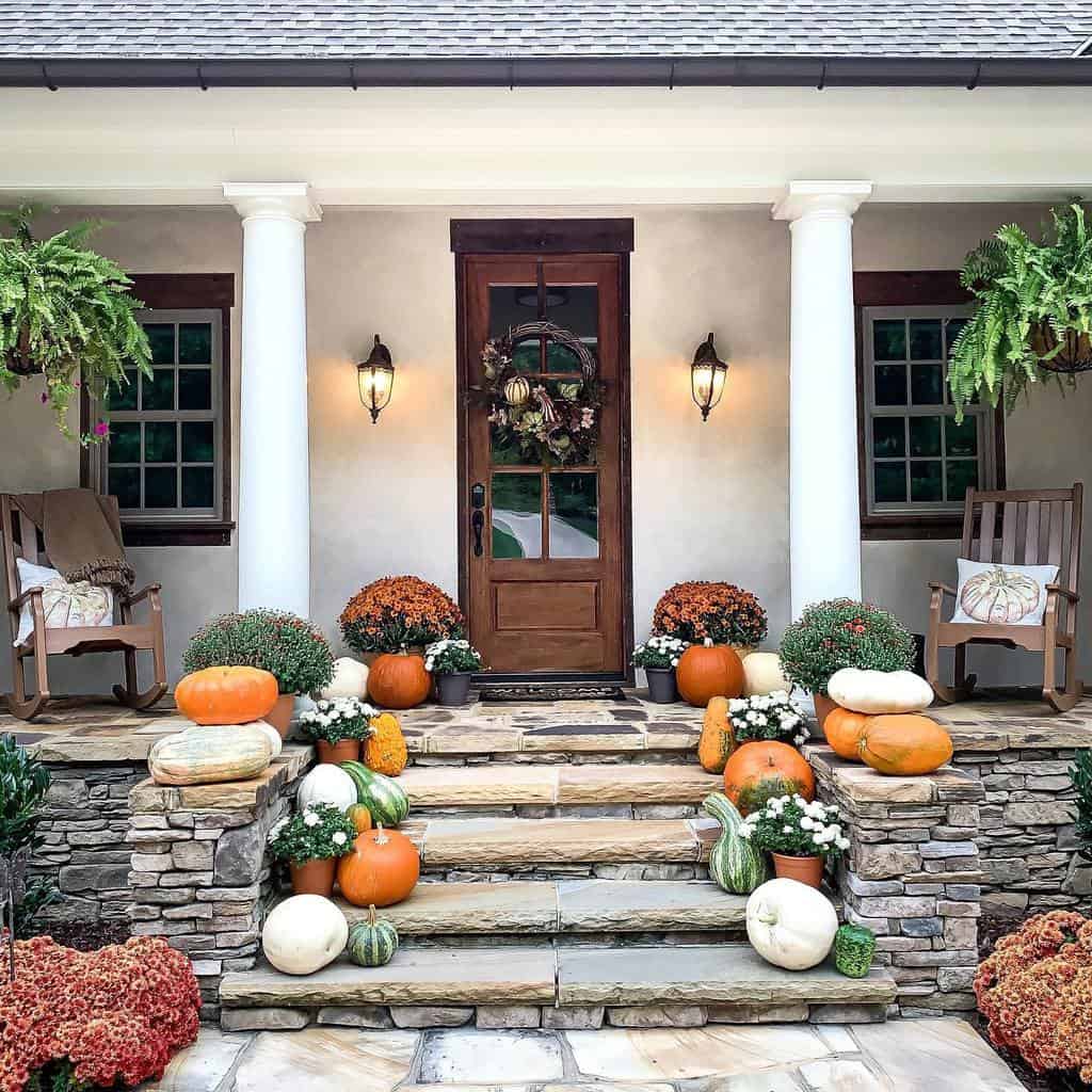 Elegant fall porch with a wooden door, stone steps, pumpkins, mums, and cozy rocking chairs, creating a warm and inviting autumn entryway