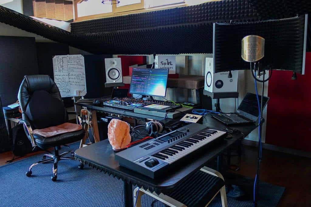 Professional music studio with a workstation, MIDI keyboard, studio monitors, acoustic panels, a recording microphone, and a cozy setup