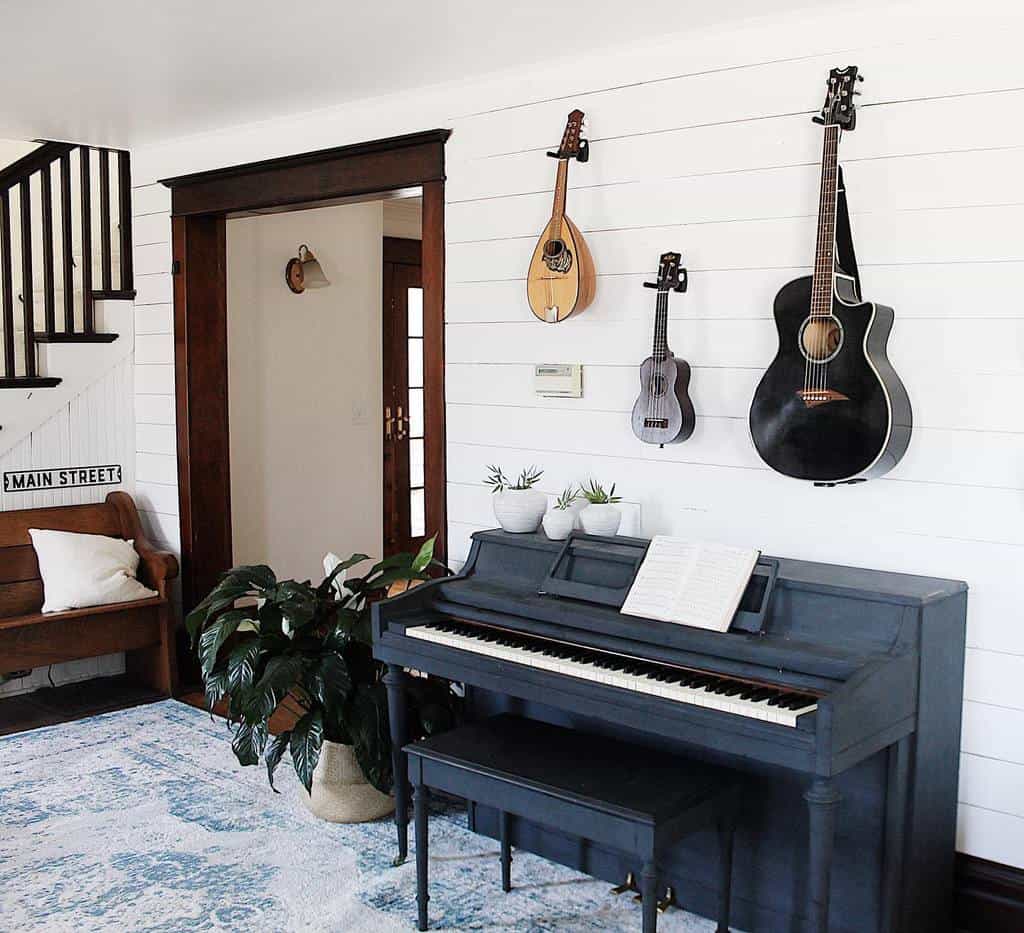 Rustic farmhouse-style music room with a black upright piano, wall-mounted string instruments, shiplap walls, and cozy vintage decor