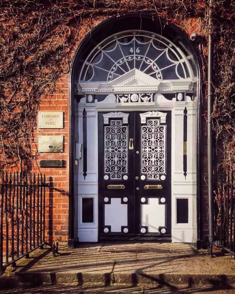 Ornate black and white front door, framed by climbing plants on a brick building