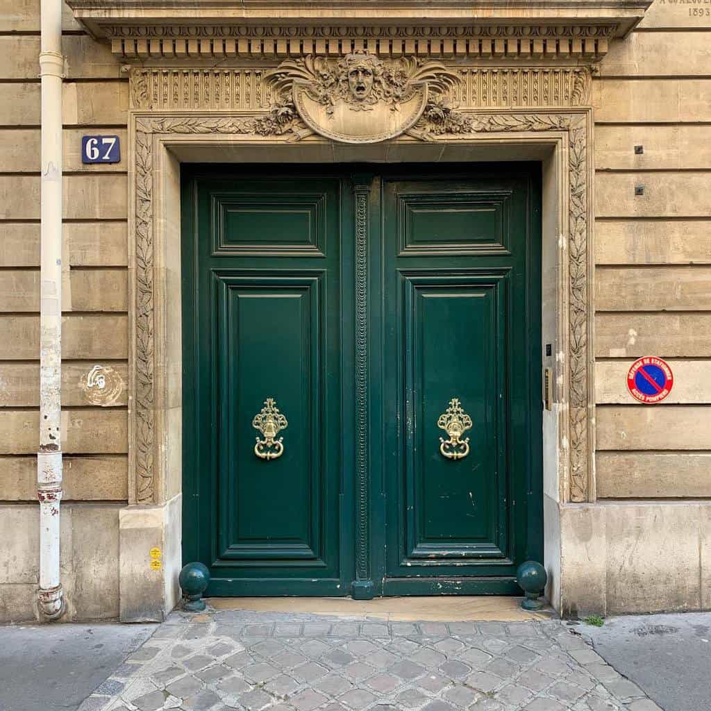 Ornate green double doors with intricate carvings and brass lion knockers set in a stone facade