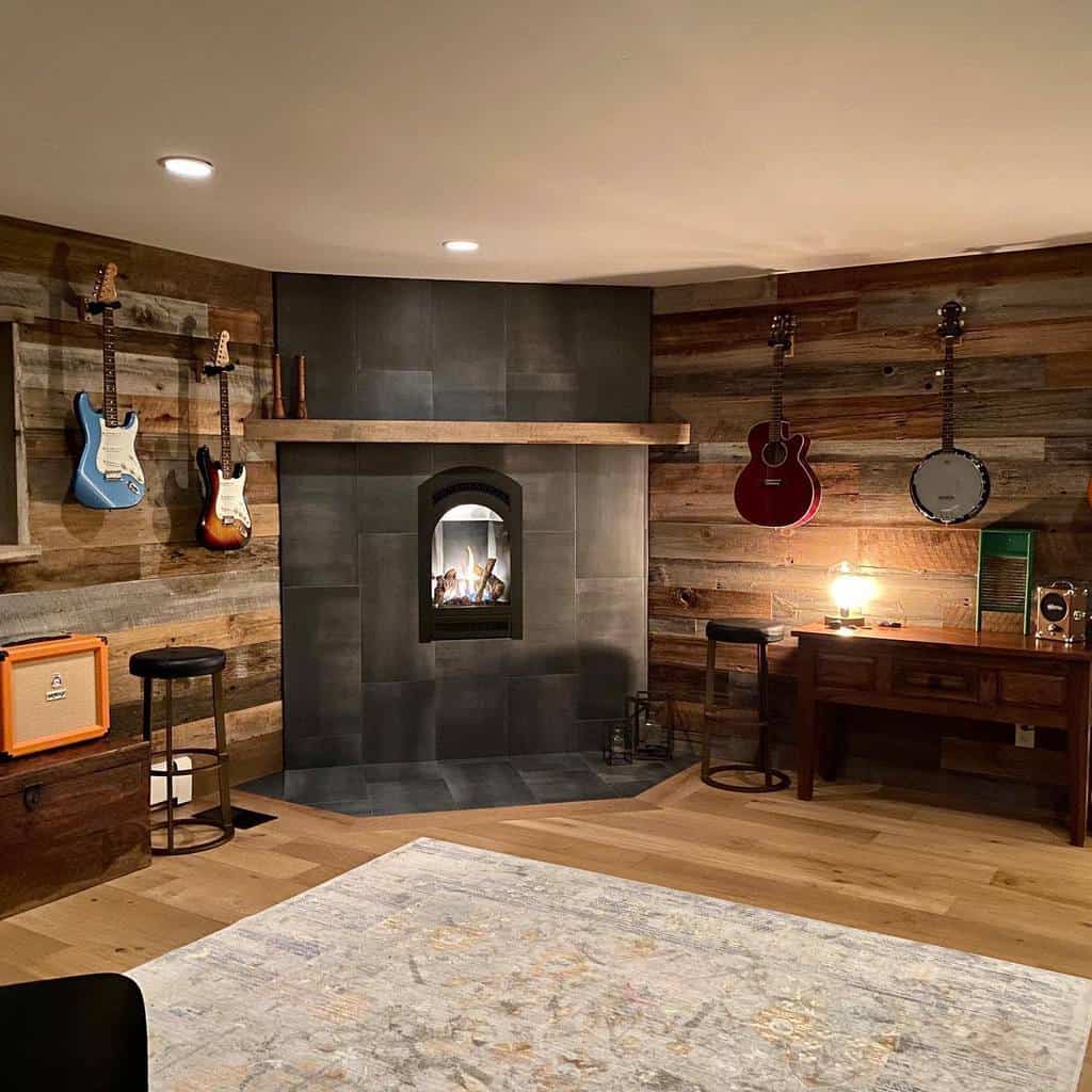 Cozy music room with a rustic wood accent wall, wall-mounted guitars, a fireplace, warm lighting, and a vintage-inspired workspace