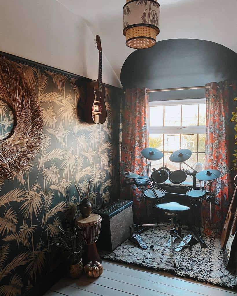 Eclectic music room with bold tropical wallpaper, an electronic drum set, a wall-mounted guitar, warm lighting, and cozy bohemian decor