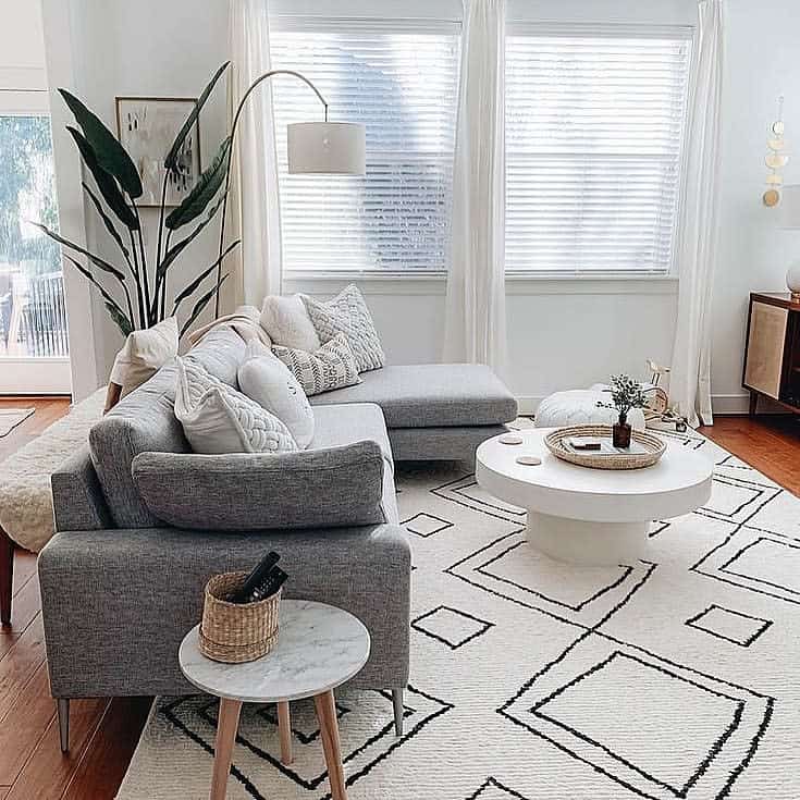 Modern round white coffee table styled with a woven tray and decor, set in a bright minimalist living room with a cozy grey sectional and geometric rug