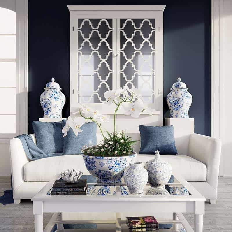 Elegant white mirrored coffee table styled with blue and white porcelain vases, orchids, and books, set in a sophisticated navy and white living room