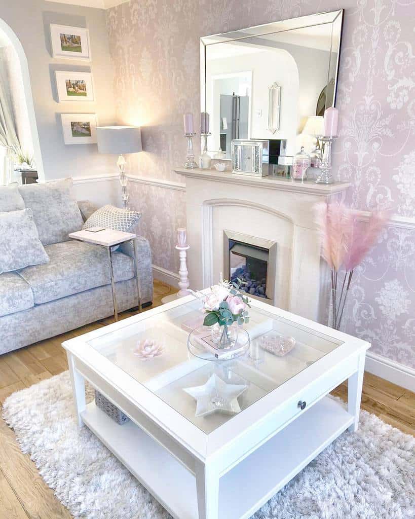 Elegant white coffee table with a glass top and lower shelf, styled with soft pink decor, flowers, and candles, set in a chic pastel-toned living room