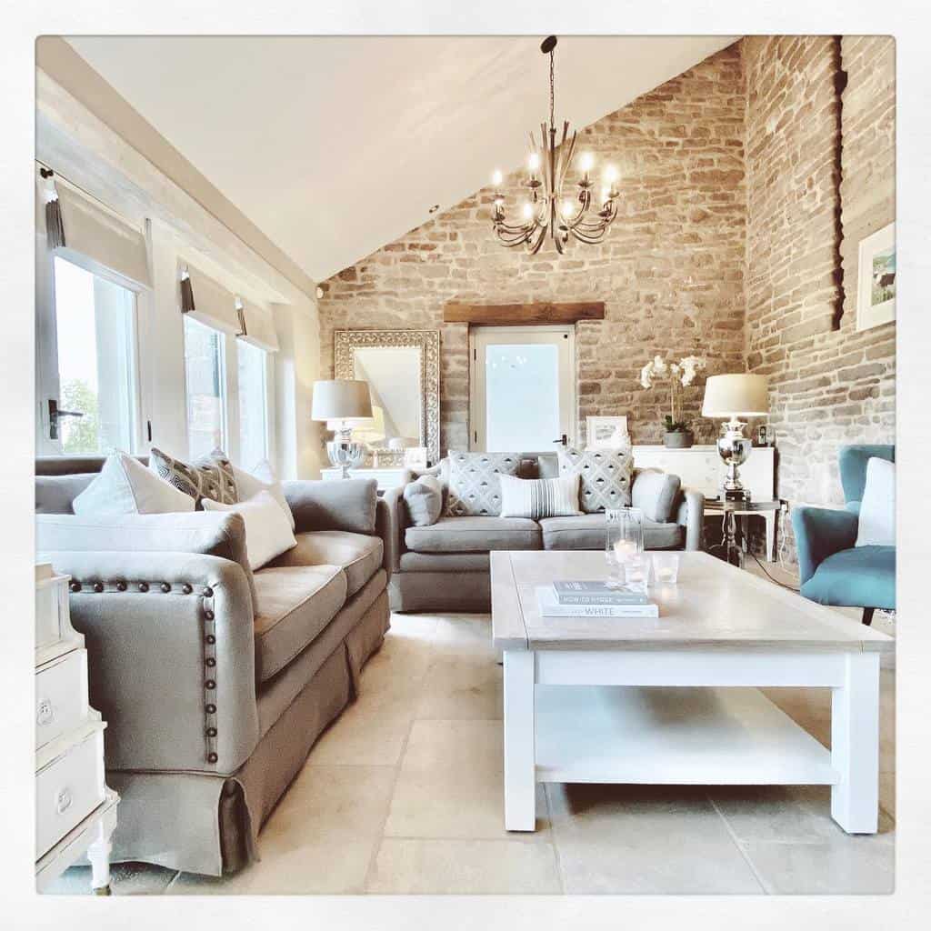 Rustic white wooden coffee table with a lower shelf, styled with books and candles, set in a cozy living room with exposed brick walls and tufted sofas