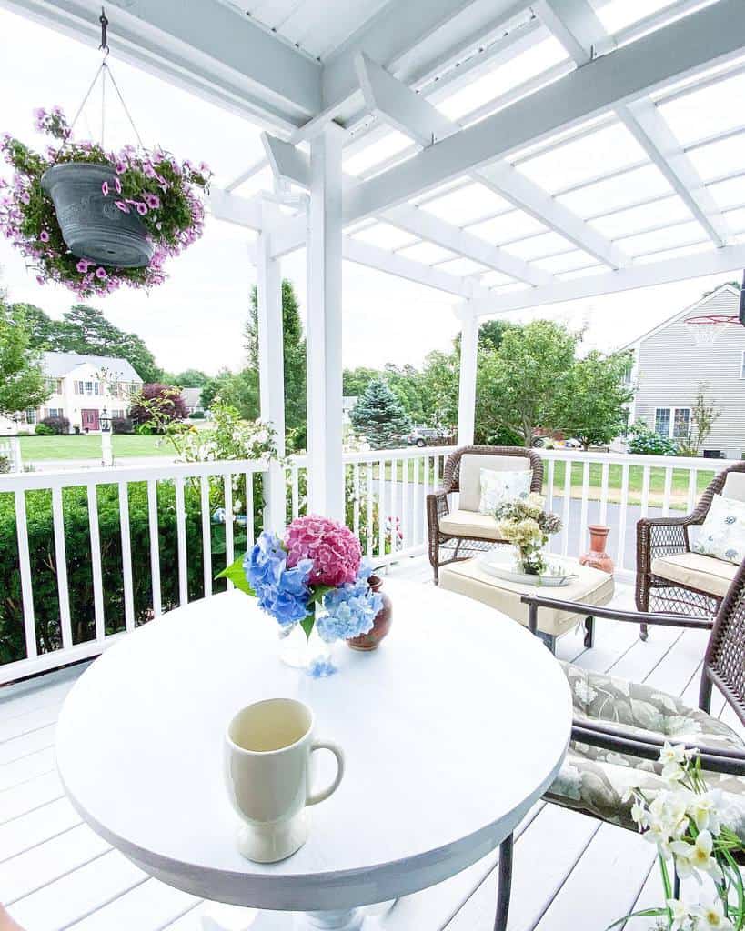 Bright and airy white porch with a pergola, cozy wicker seating, floral accents, and a charming table setup for a relaxing outdoor retreat