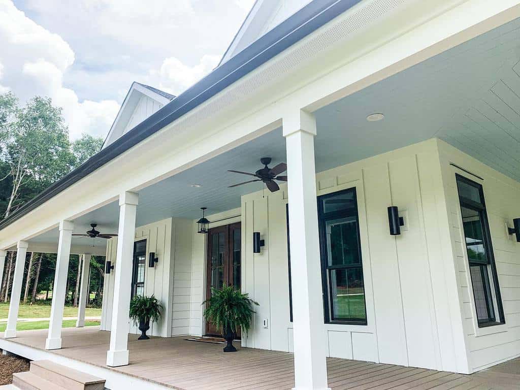 Front porch of a modern white house with columns, dark window frames, ceiling fans, and potted plants