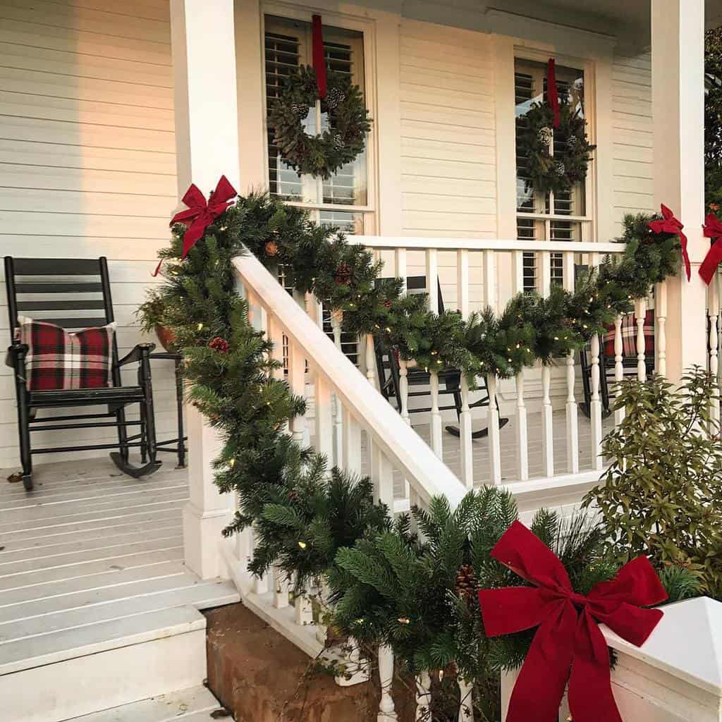 Front porch with festive Christmas garlands and red bows on railing, and two rocking chairs with plaid cushions by the window