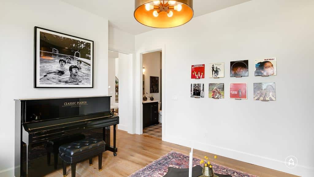 Elegant music room with a black upright piano, vinyl records displayed on the wall, a Beatles-themed artwork, and warm modern lighting