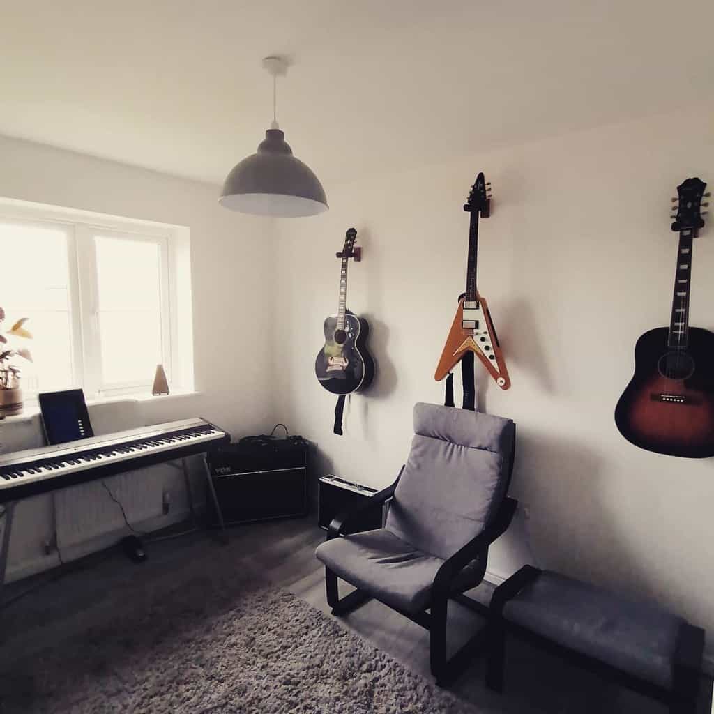 Minimalist music room with wall-mounted guitars, a digital piano, a Vox amplifier, a cozy gray chair, and soft natural lighting