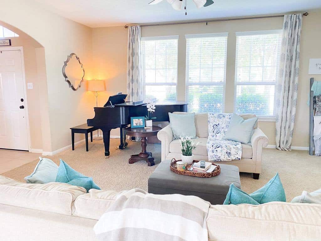 Bright living room with a grand piano, cozy couches, blue and white decor, and a large window letting in natural light