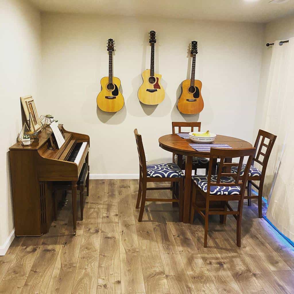 A cozy room with a piano and sheet music, three acoustic guitars on the wall, and a round table with chairs on a wooden floor