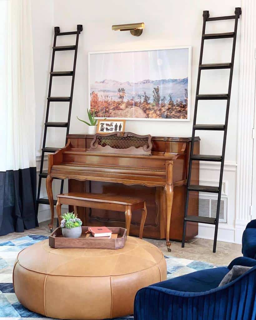 A wooden piano with a nature photo above, flanked by two black ladders, and a brown ottoman with a tray of plants in the foreground