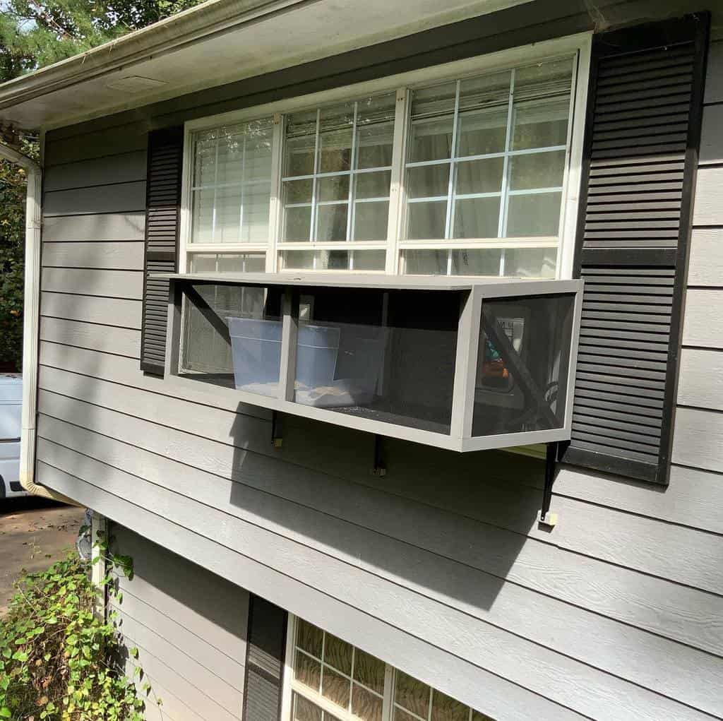 Compact window catio with a sturdy black frame, mesh sides, and a secure outdoor perch, providing fresh air and a view for indoor cats