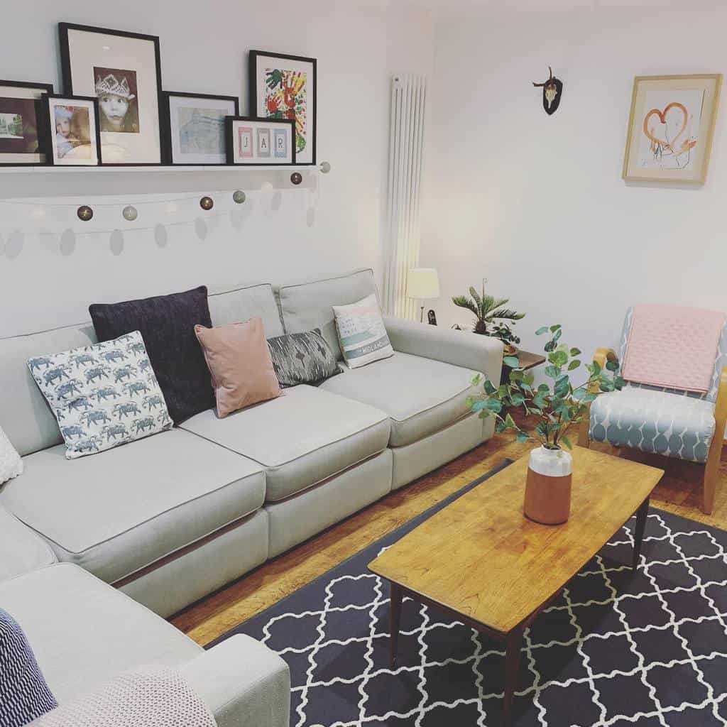 Cozy living room with a gray sofa, assorted pillows, simple wooden coffee table, decorative artwork, and a patterned rug