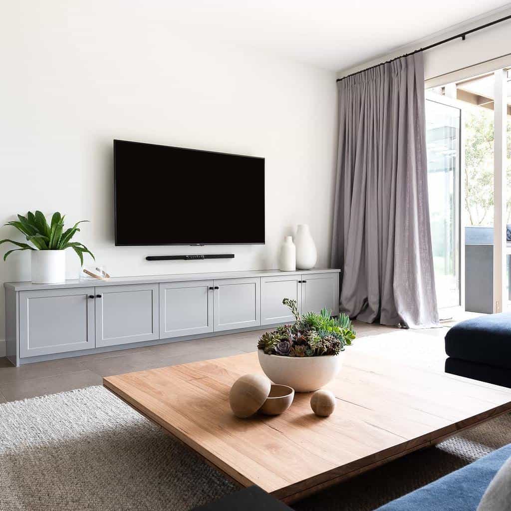 Modern low-profile wooden coffee table styled with a ceramic planter and decorative spheres, set in a minimalist living room with neutral tones