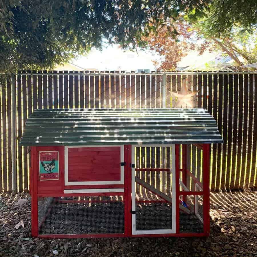 Compact red and white chicken coop with a green metal roof, mesh-enclosed run, and a vintage-style 'Fresh Eggs' sign